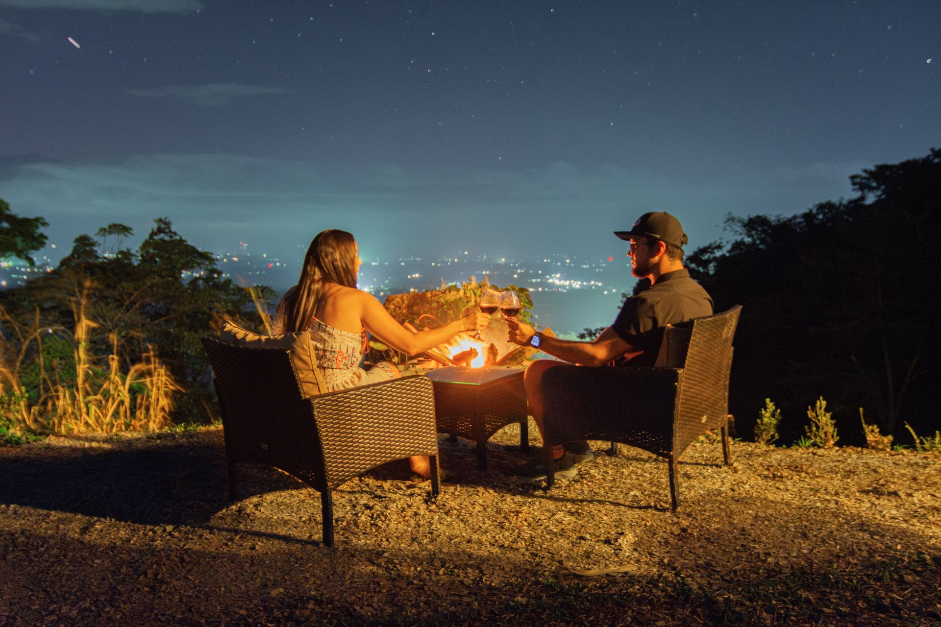 Pareja brindando junto a la fogata exterior con el valle iluminado de noche
