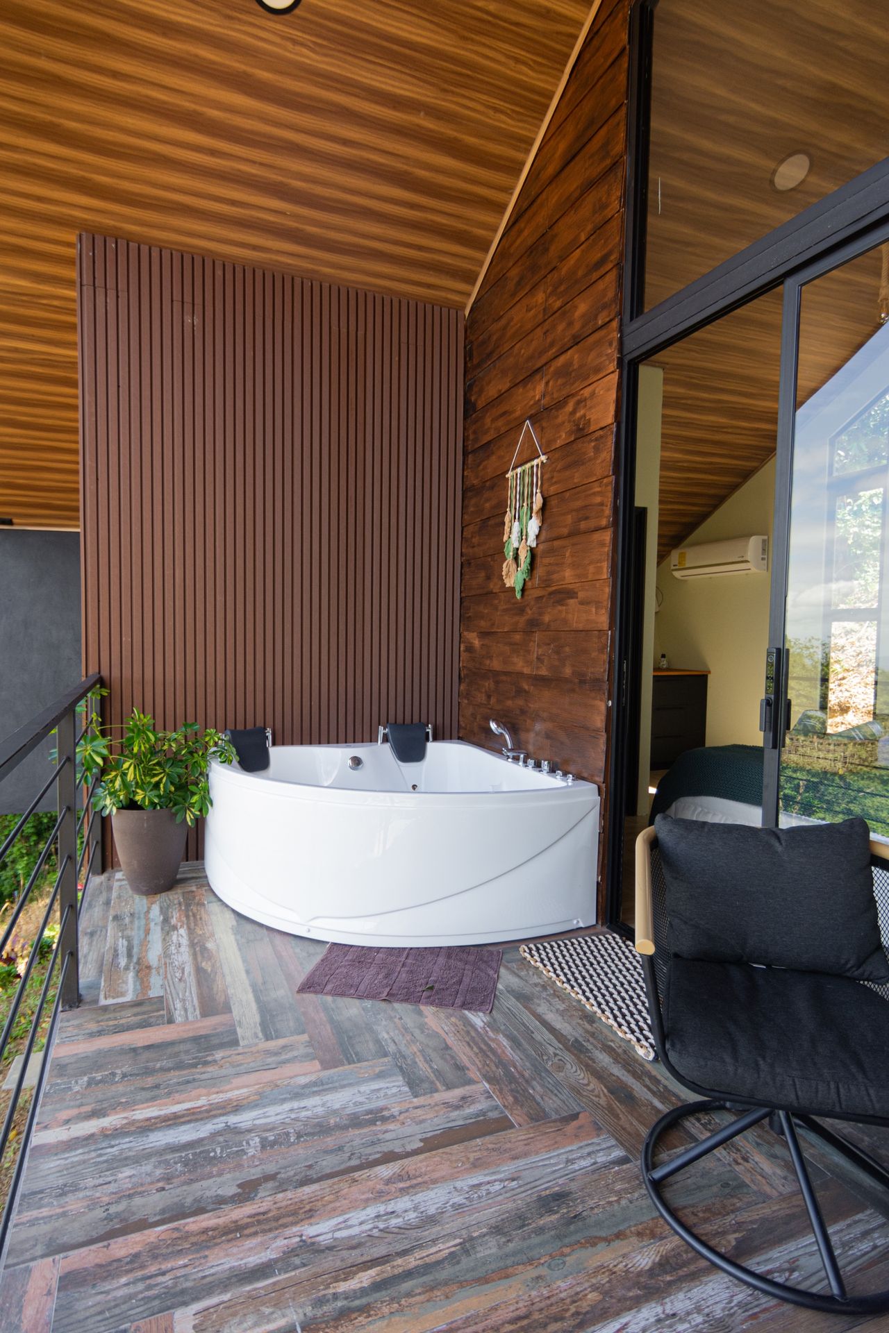 Jacuzzi blanco en el balcón techado con piso de madera y sillón